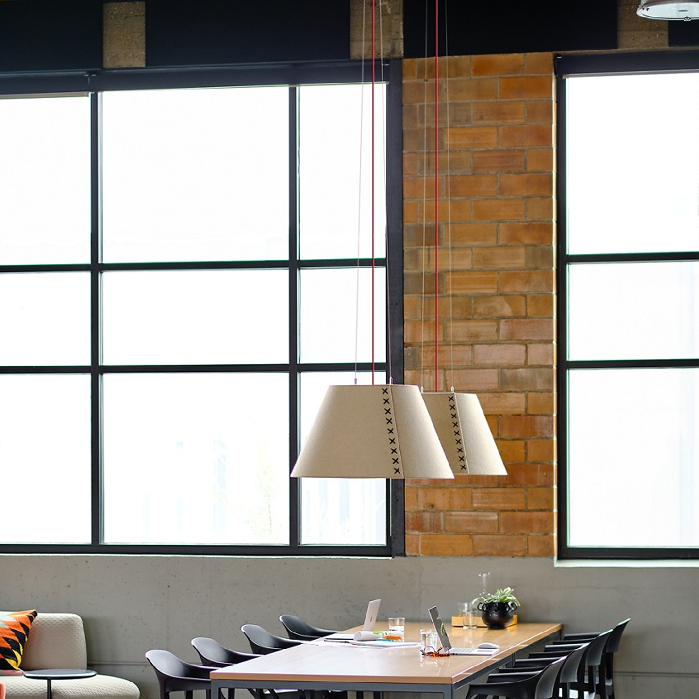 Haworth BuzziShade lighting in white above office collaboration area with table and black chairs 