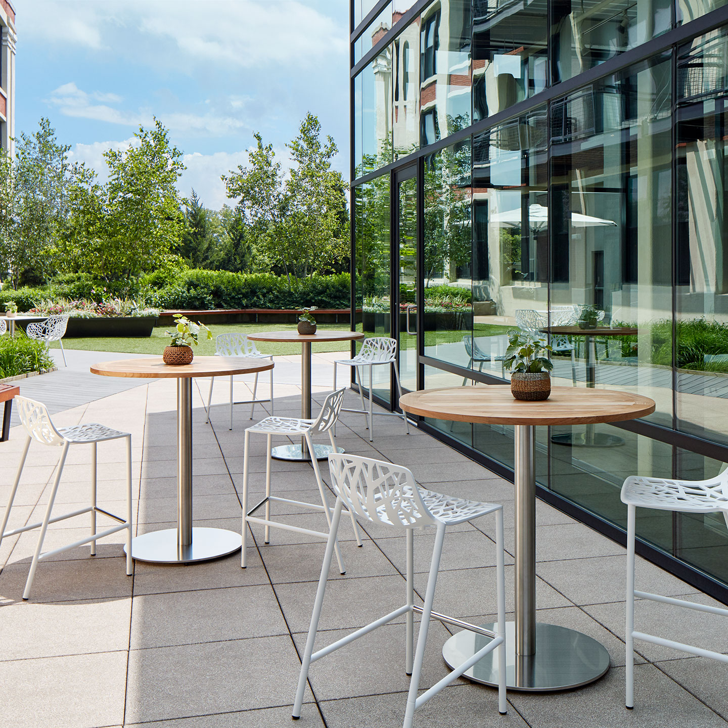 Haworth Janus Cafe Table with Natural Teak Wood top and circular base in outdoor seating seating with tall chairs and glass windows.