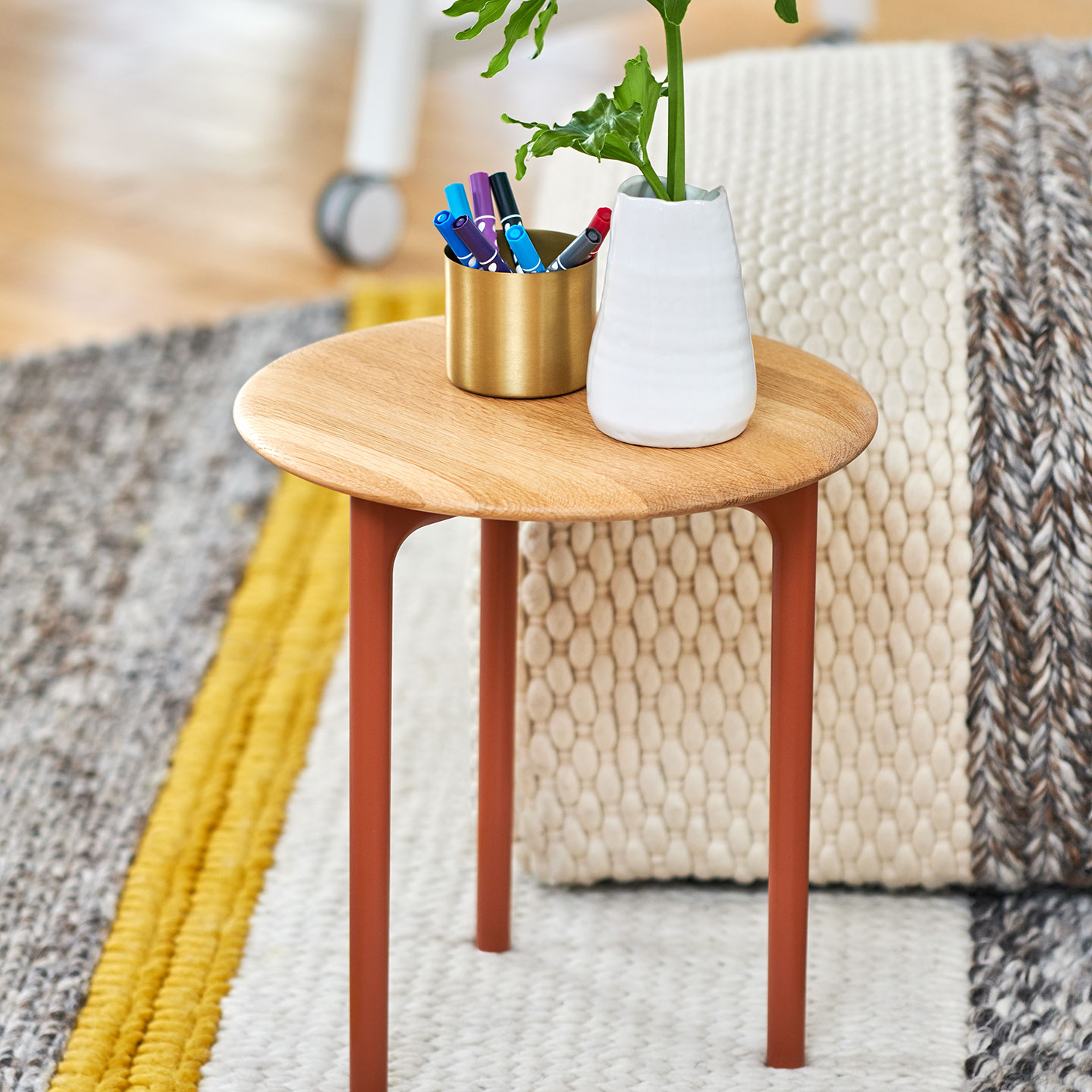 Haworth Openest Sprig Side Table with White Oak Hardwood circular top next to an ottoman with a plant and pens on it